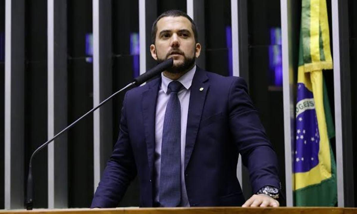Carlos Jordy falando em microfone com expressão séria