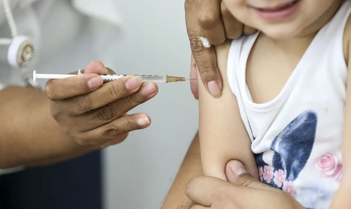 Criança sendo vacinada no braço sem mostrar o rosto inteiro