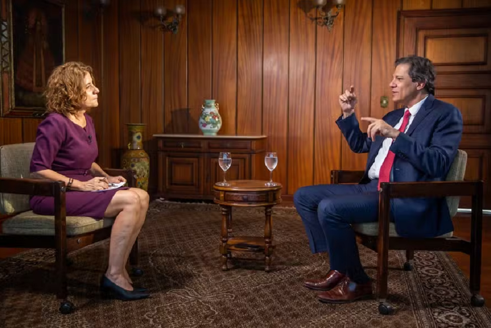 Miriam Leitão e Fernando Haddad sentados, frente à frente, ele falando e gesticulando