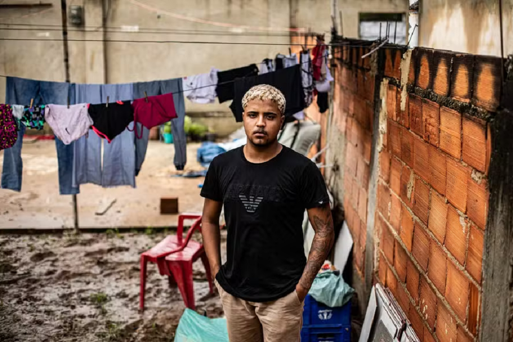 Marcos Vinicius de Souza posando em pé, com expressão séria, de camiseta preta e bermuda bege