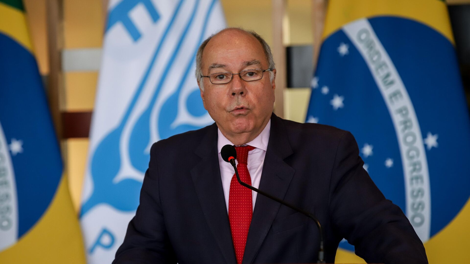 Mauro Vieira falando em microfone com expressão séria