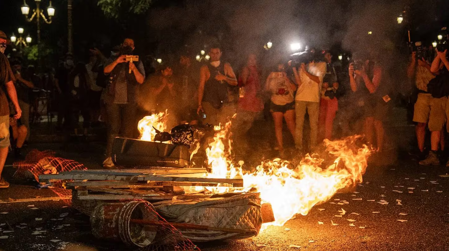 Colchão pegando fogo na rua com manifestantes em volta