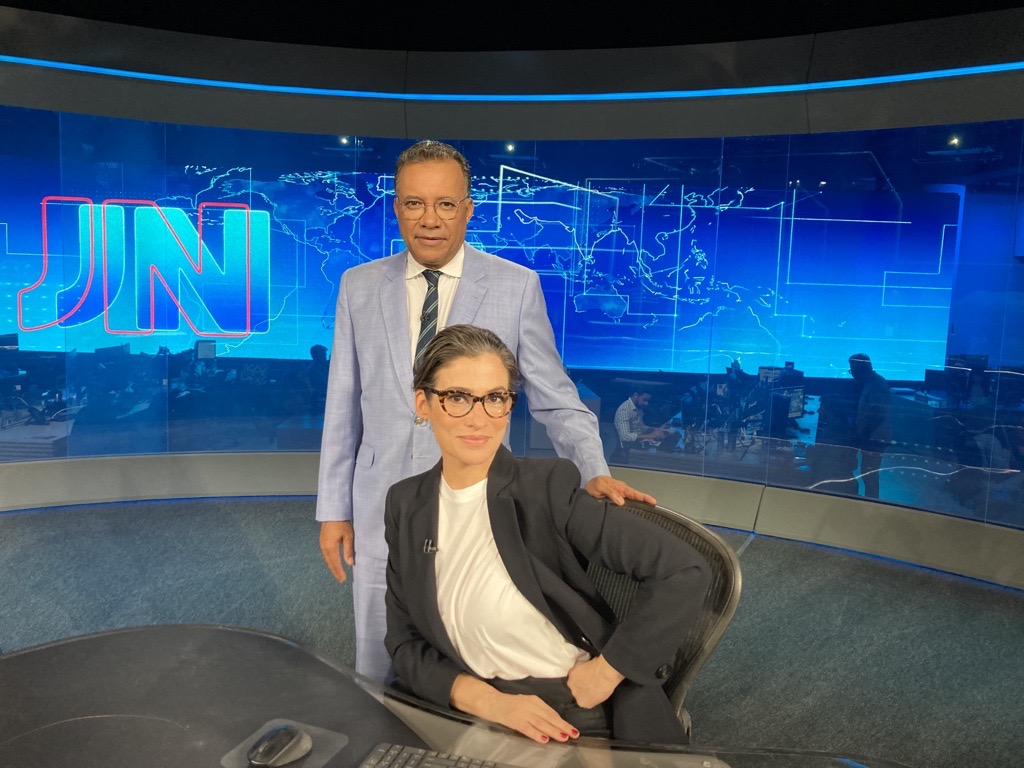 Haroldo Pereira e Renata Vasconcellos posando sorridentes no estúdio do Jornal Nacional