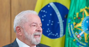 Lula de perfil, sorrindo, perto de bandeira brasileira