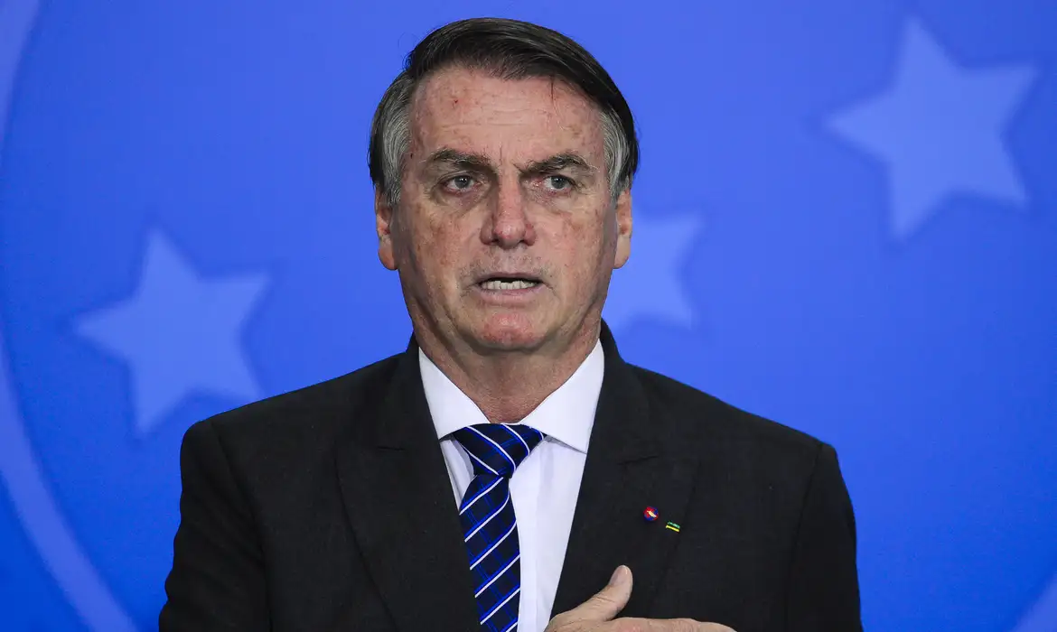 Jair Bolsonaro com expressão desconfiada e mão no peito