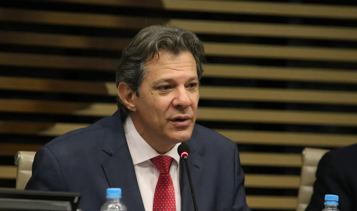 Fernando Haddad falando com expressão séria, sem olhar pra câmera, de roupa social
