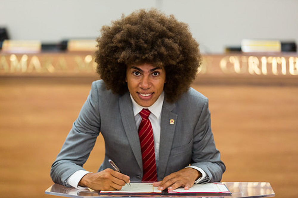 Renato Freitas sorrindo, olhando pra câmera e assinando livro