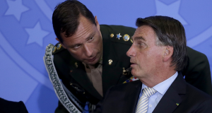 Mauro Cid abaixado e conversando com Jair Bolsonaro, os dois sérios