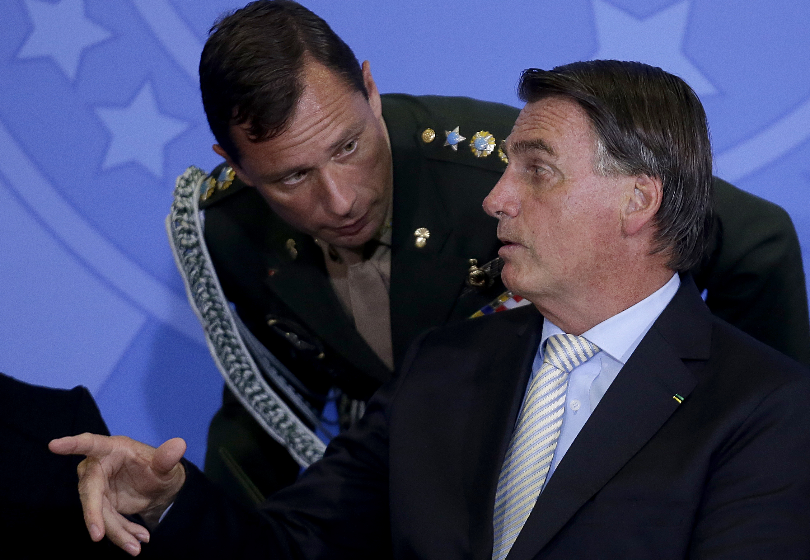 Mauro Cid abaixado e conversando com Jair Bolsonaro, os dois sérios