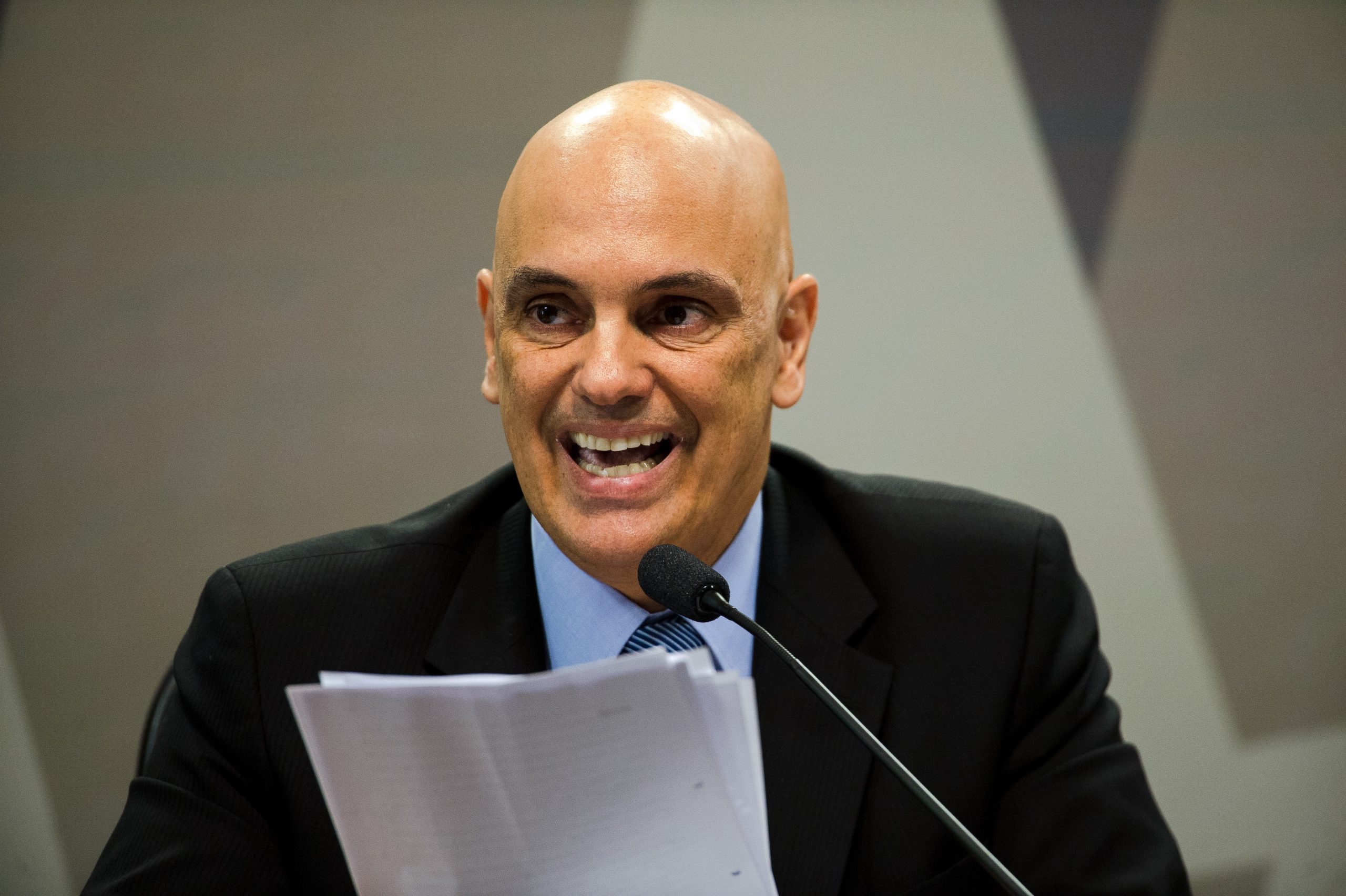 Alexandre de Moraes fazendo careta, perto de microfone, sem olhar para a câmera