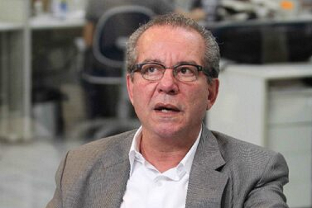 José Aníbal de roupa social cinza e branca, com óculos, falando e olhando para cima