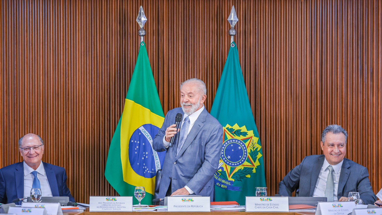 Lula falando em microfone e sorrindo, em pé