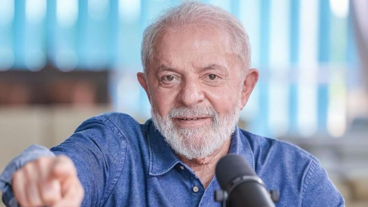 Lula de camisa jeans, apontando para frente e sorrindo