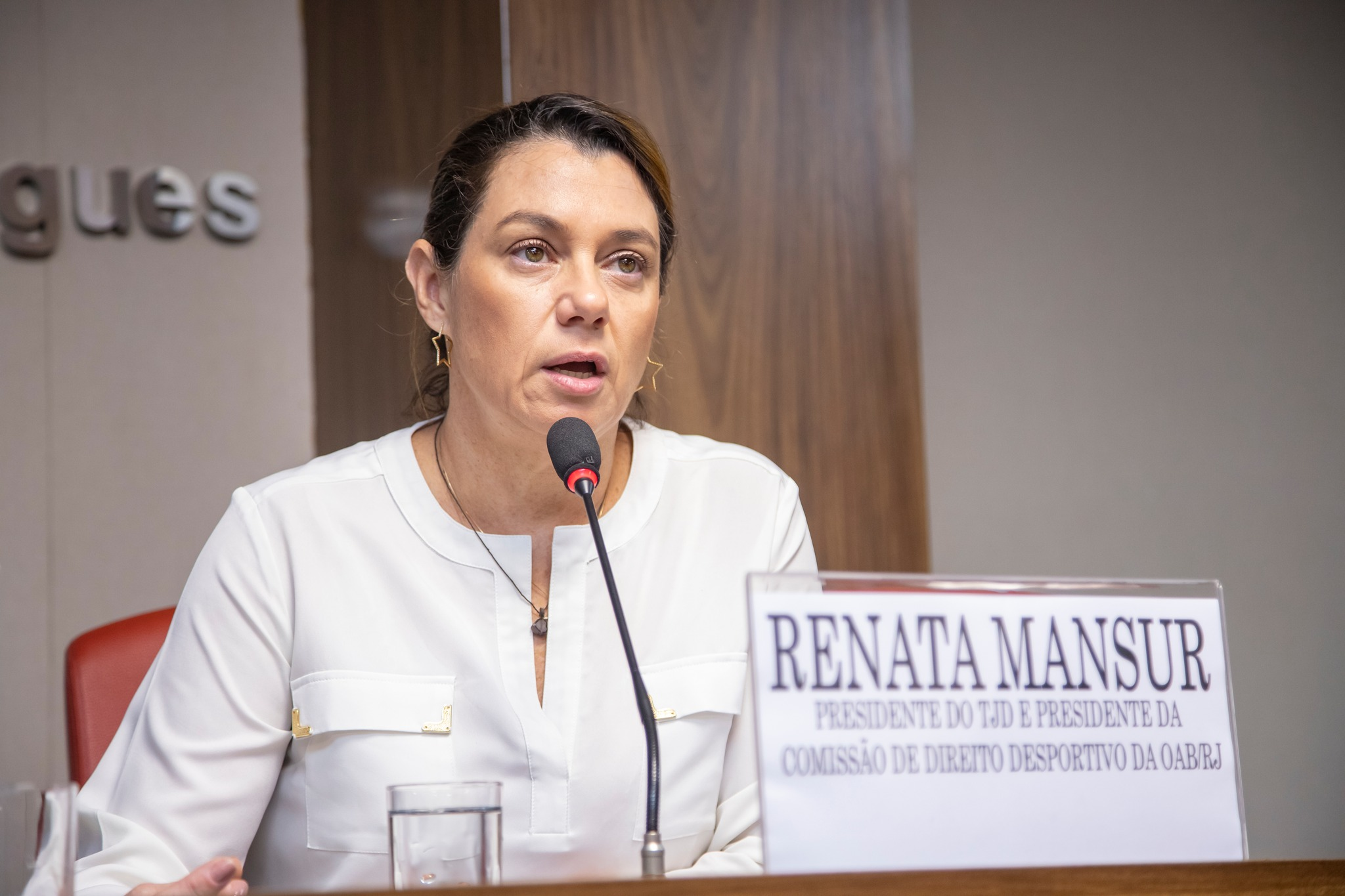 Renata Mansur de roupa branca e cabelo preso, falando com expressão séria