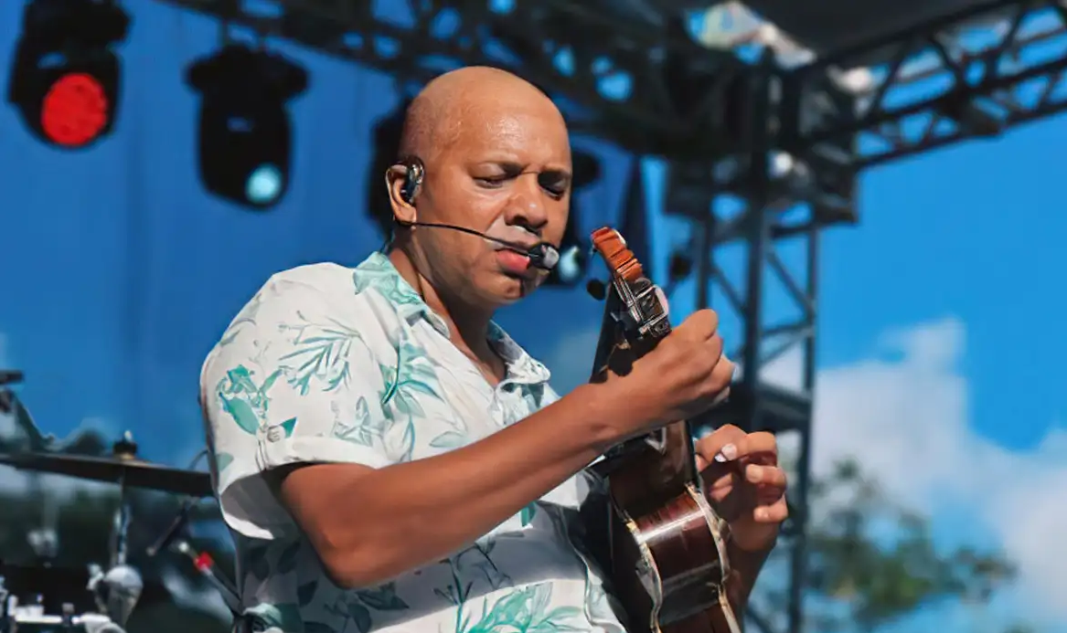 Anderson Leonardo cantando e tocando cavaquinho, com camisa estampada azul e branca