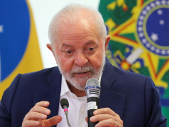 Lula falando em microfone com bandeiras ao fundo