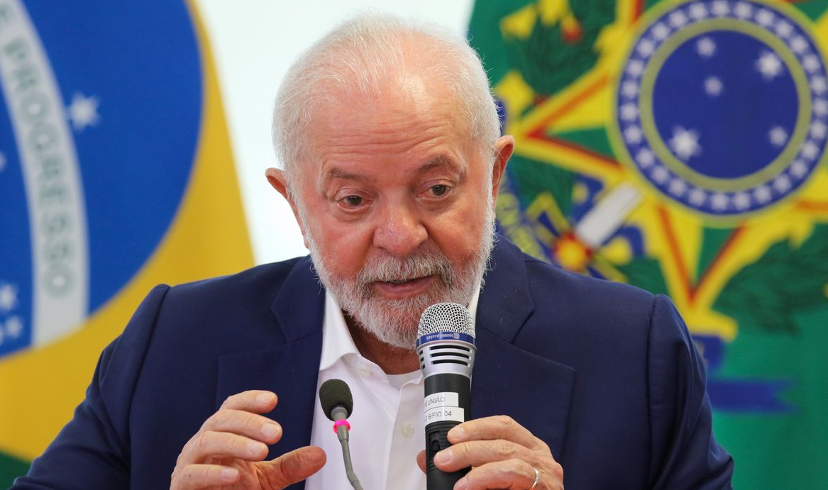 Lula falando em microfone com bandeiras ao fundo