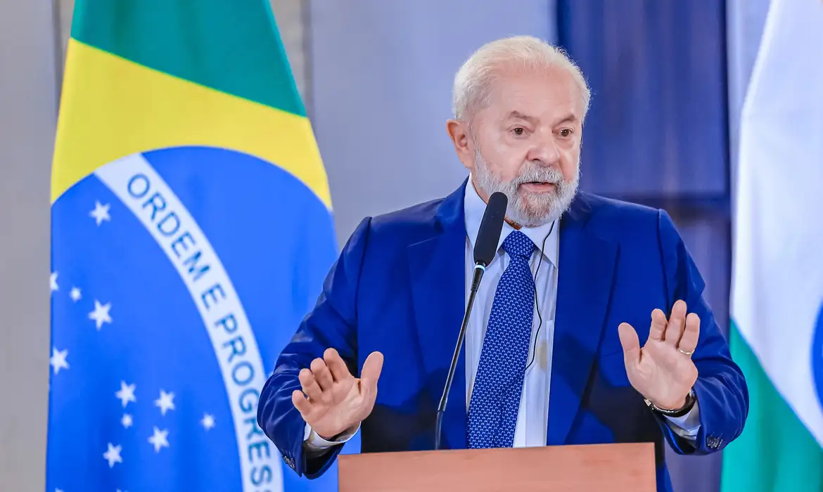 Lula falando e gesticulando com bandeira do Brasil ao fundo