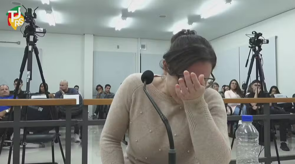Yasmin Vaz dos Santos Rodrigues de blusa bege e cabeça baixa, perto de microfone, com rabo de cavalo