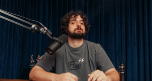 Monark posando para foto em estúdio, com expressão séria e camiseta cinza do Flow