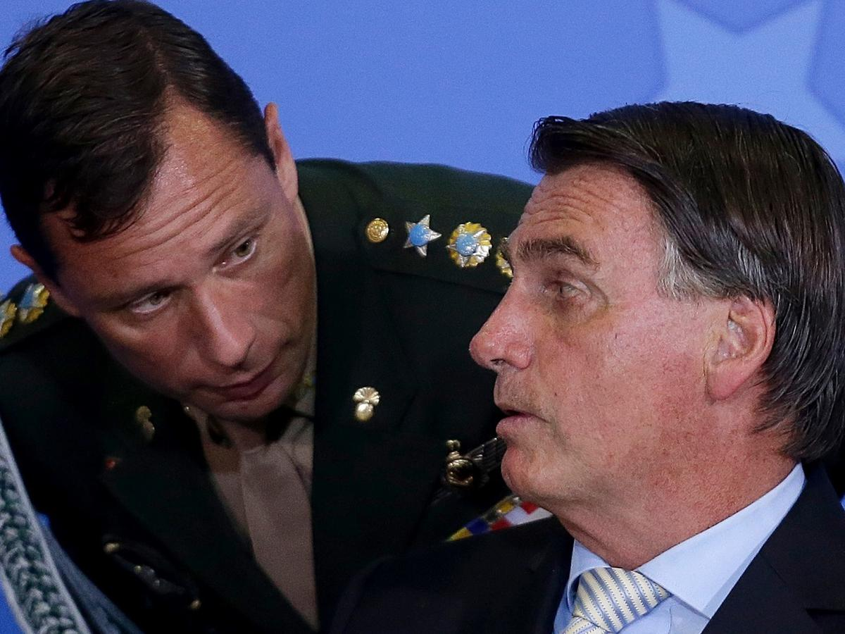 Mauro Cid abaixado e ouvindo Jair Bolsonaro falar