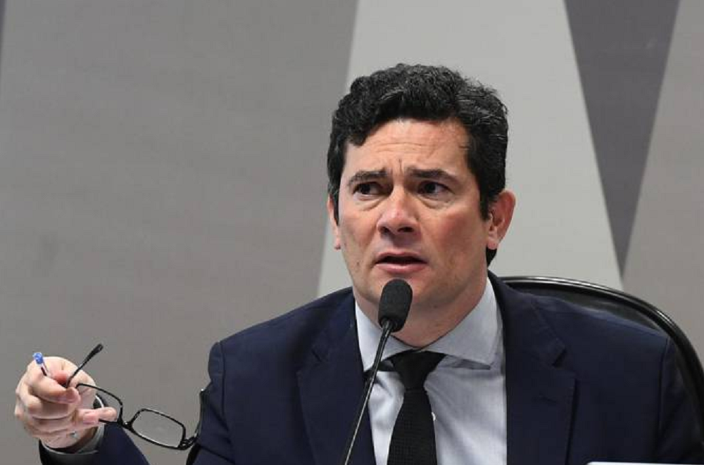 Sergio Moro com expressão de desconfiança, segurando óculos