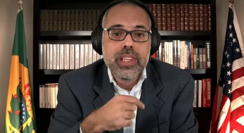Allan dos Santos de óculos e fones de ouvido, falando para a câmera