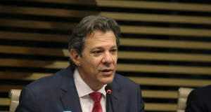 Fernando Haddad falando em microfone com expressão séria, sem olhar pra câmera