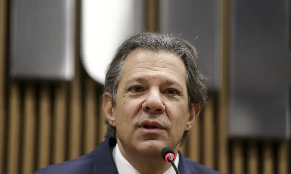 Fernando Haddad com expressão séria, falando em microfone