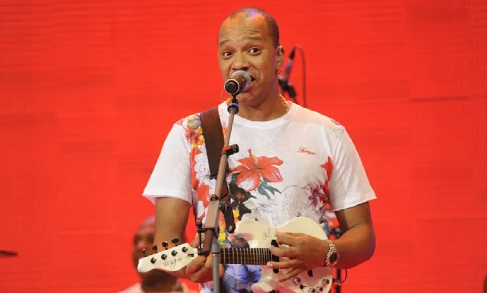 Anderson Leonardo cantando e tocando, foto com fundo vermelho