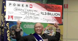 Cheng Saephan sorrindo e levantando cheque bilionário da loteria dos EUA
