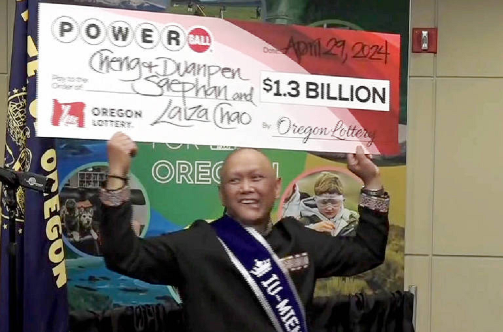 Cheng Saephan sorrindo e levantando cheque bilionário da loteria dos EUA