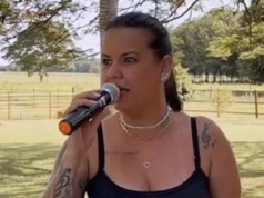 Nanda Ferraz cantando em microfone, de camiseta preta e rabo de cavalo, olhando para o lado