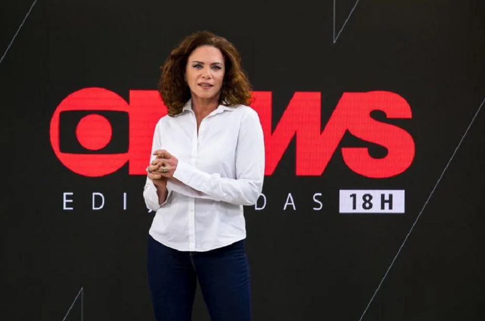 Leilane Neubarth de calça jeans e camisa social branca, de cabelo solto, séria