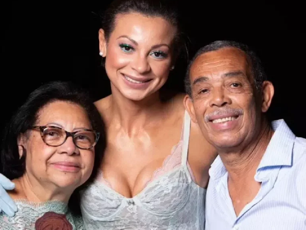 Walewska Oliveira sorrindo entre a mãe e o pai