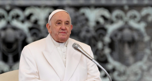 Papa Francisco com as mãos unidas, perto de microfone, sem sorrir e sem olhar para a câmera