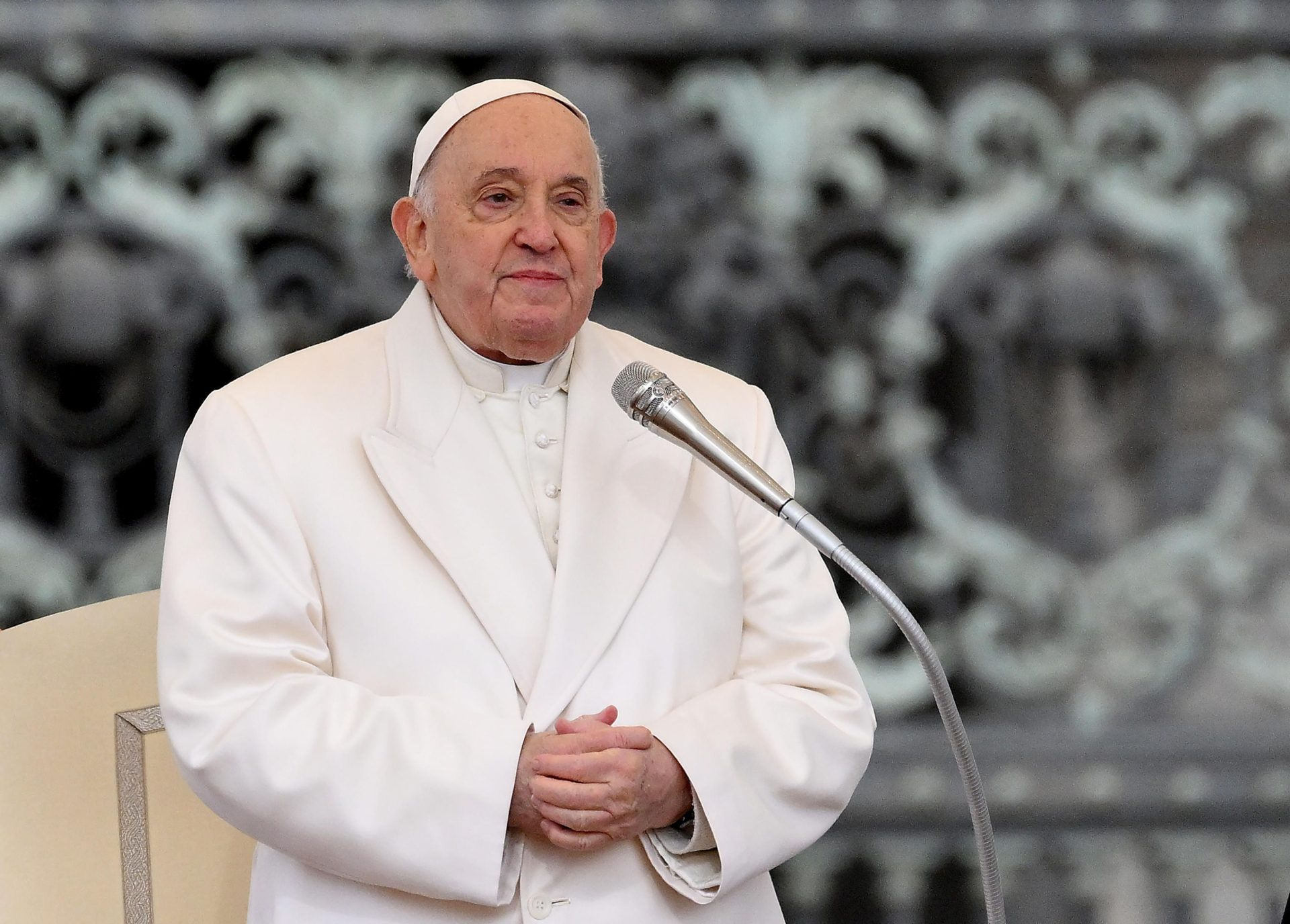 Papa Francisco com as mãos unidas, perto de microfone, sem sorrir e sem olhar para a câmera