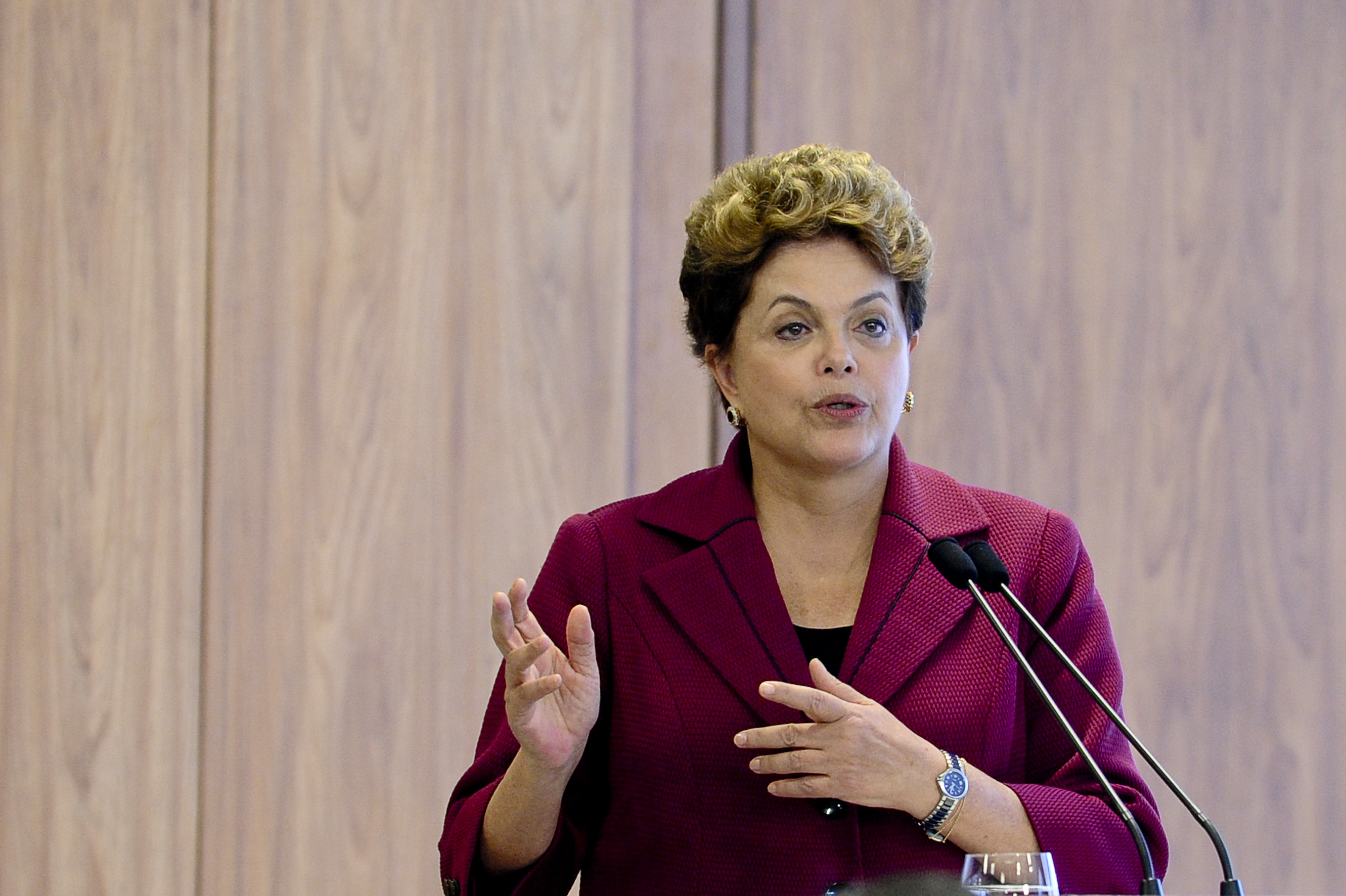 Dilma Rousseff falando e gesticulando com roupa cor de vinho