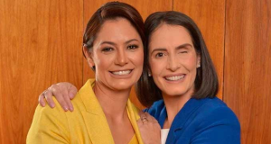 Michelle Bolsonaro e Amália Barros posando para foto abraçadas e sorrindo, a primeira de amarelo e a segunda de azul