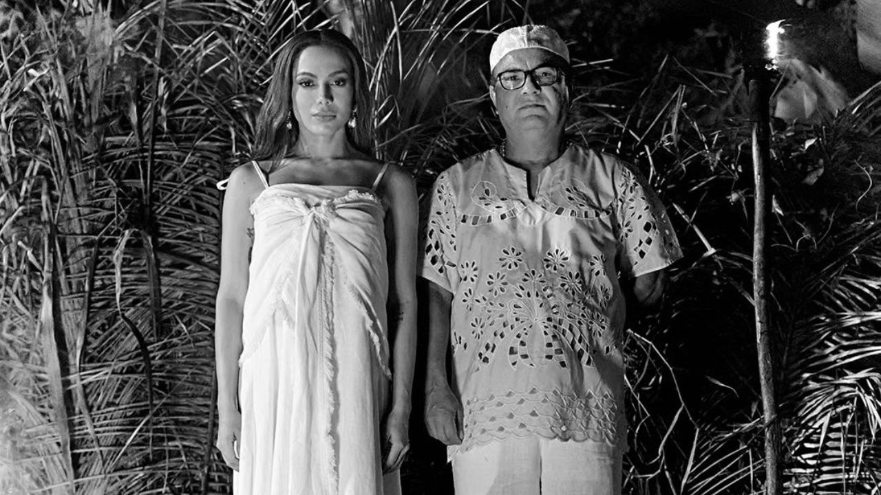Anitta em pé de roupa branca ao lado de homem em foto em preto e branco