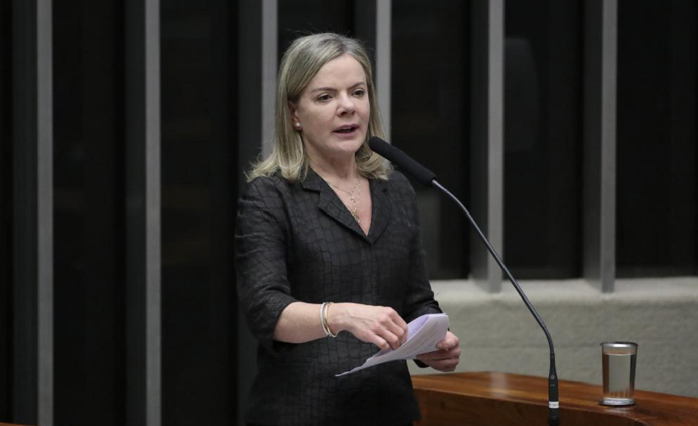 Gleisi Hoffmann de roupa preta, em pé, falando em microfone e segurando papel, na Câmara dos Deputados