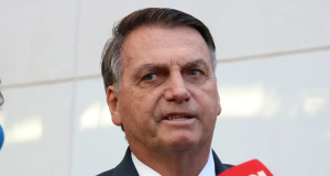 Jair Bolsonaro falando em vários microfones e fazendo careta