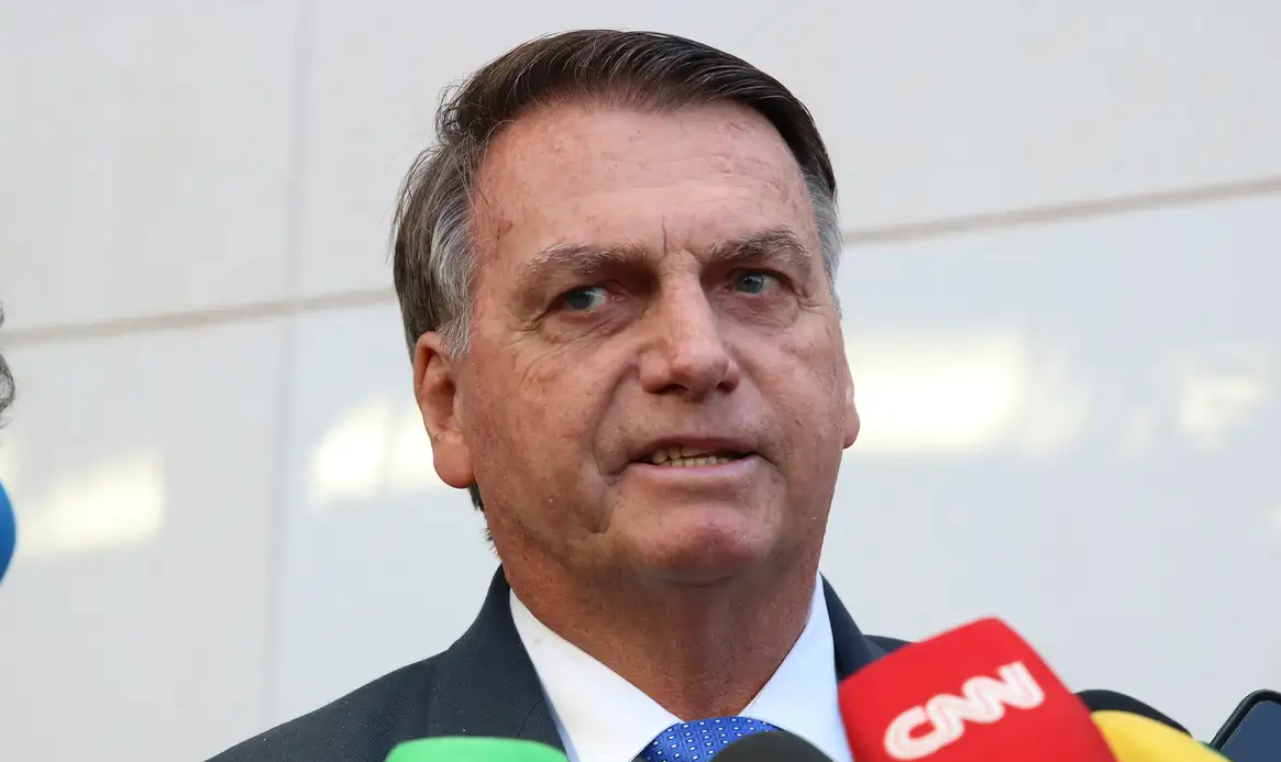 Jair Bolsonaro falando em vários microfones e fazendo careta
