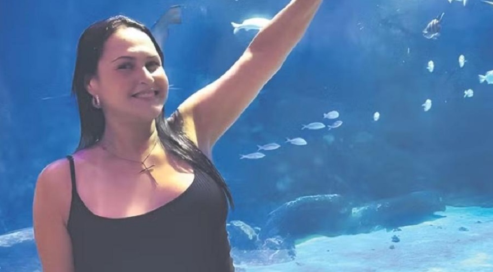 Anic de Almeida Peixoto Herdy de camiseta preta, sorrindo, com braço levantado, perto de aquário