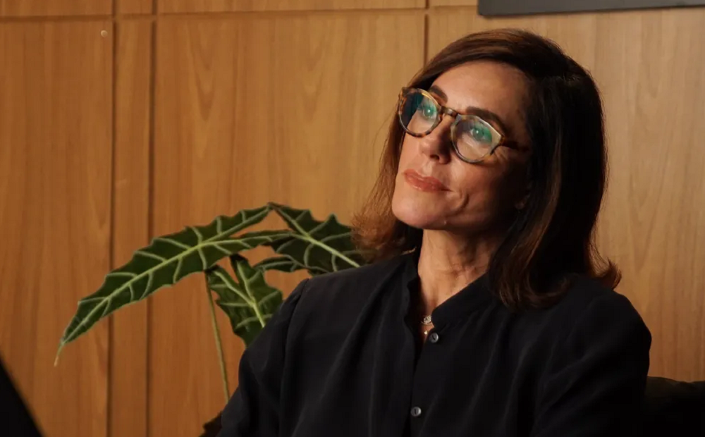 Christiane Torloni de perfil, roupa preta e óculos, séria