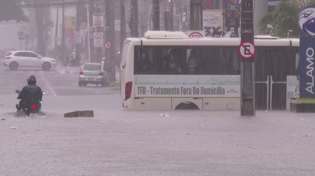 Cruzamento entre as avenidas Dom Pedro II e Coremas, no Centro de João Pessoa, alagado, com ônibus e moto passando em sentidos diferentes