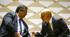 Flávio Dino e Alexandre de Moraes conversando, ambos sentados e próximos, de roupa social