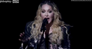 Madonna de roupa preta e cabelo solto, cantando em microfone