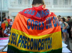 Pessoa com bandeira contra o preconceito, de costas, perto de multidão