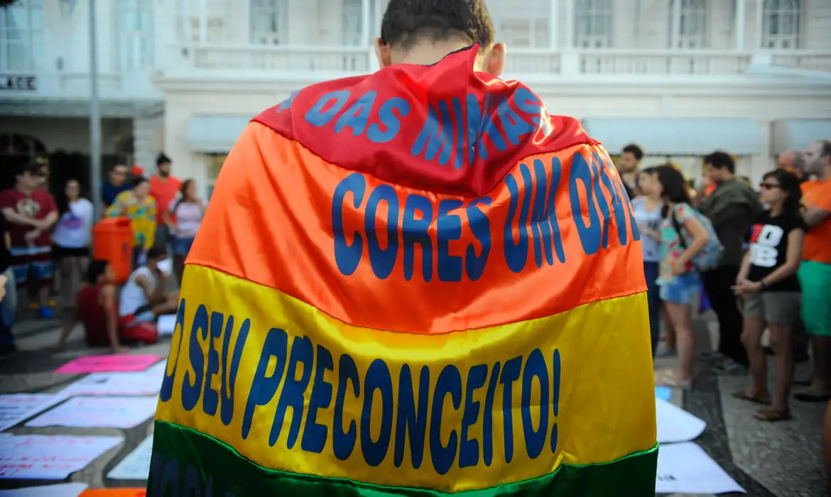 Pessoa com bandeira contra o preconceito, de costas, perto de multidão